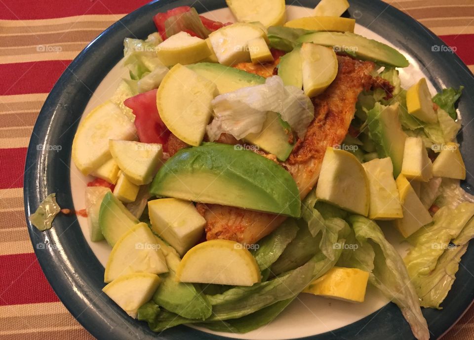 Colorful salad loaded with veggies, including cucumbers, lettuce, zuchinni, summer squash, avacado, tomatoes and salmon.