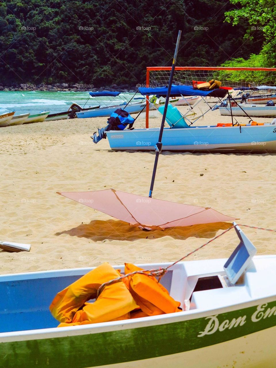 Beautiful colorful photo of a Beach, with boats and an pink umbrella. We can see the blue sea and the yellow beach sand.