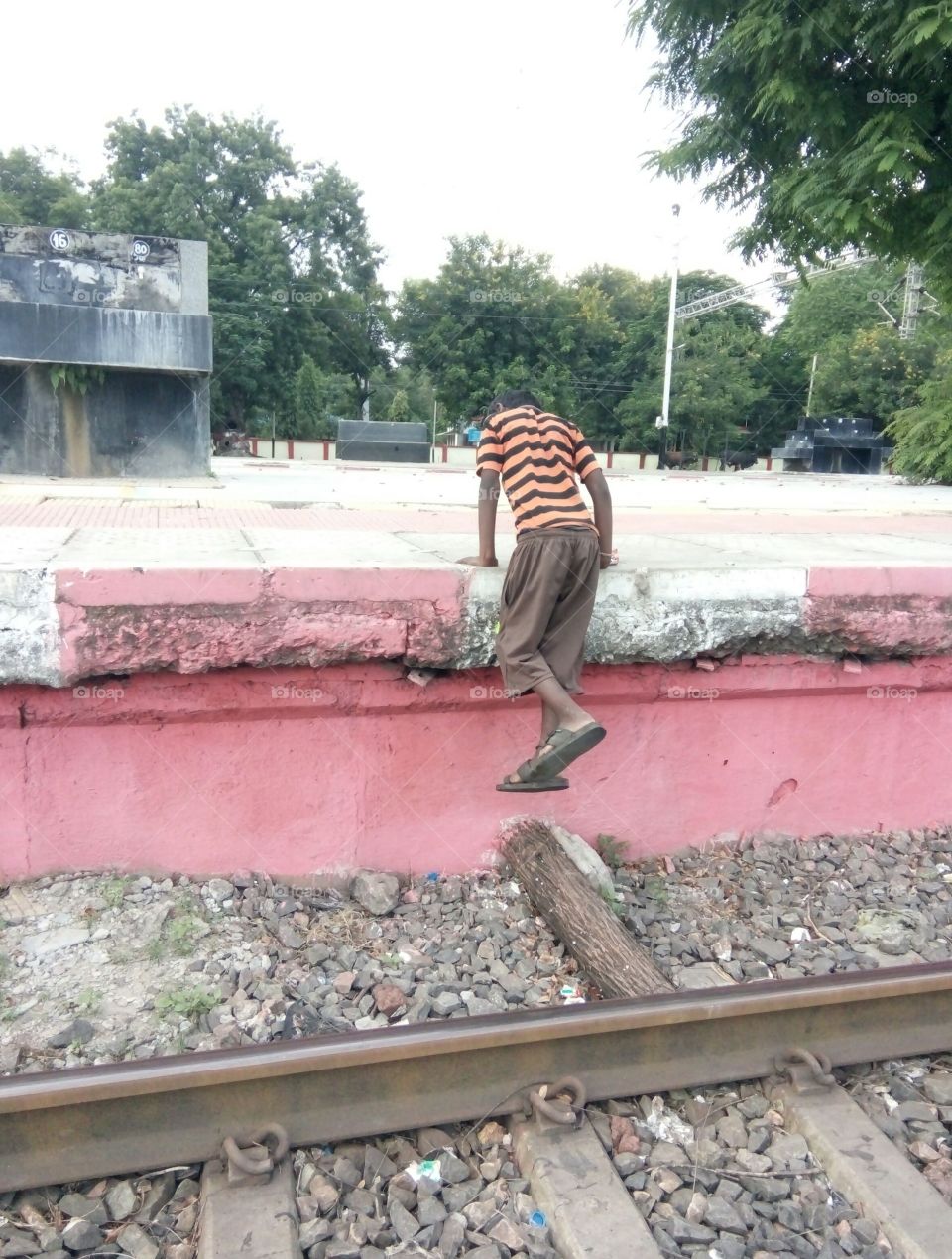 Photo of a boy / little boy walking up / Photo of an Indian boy / poor boy walking on a platform / A photo of a boy in a red and black t shirt/Pictures of a boy walking at a railway station