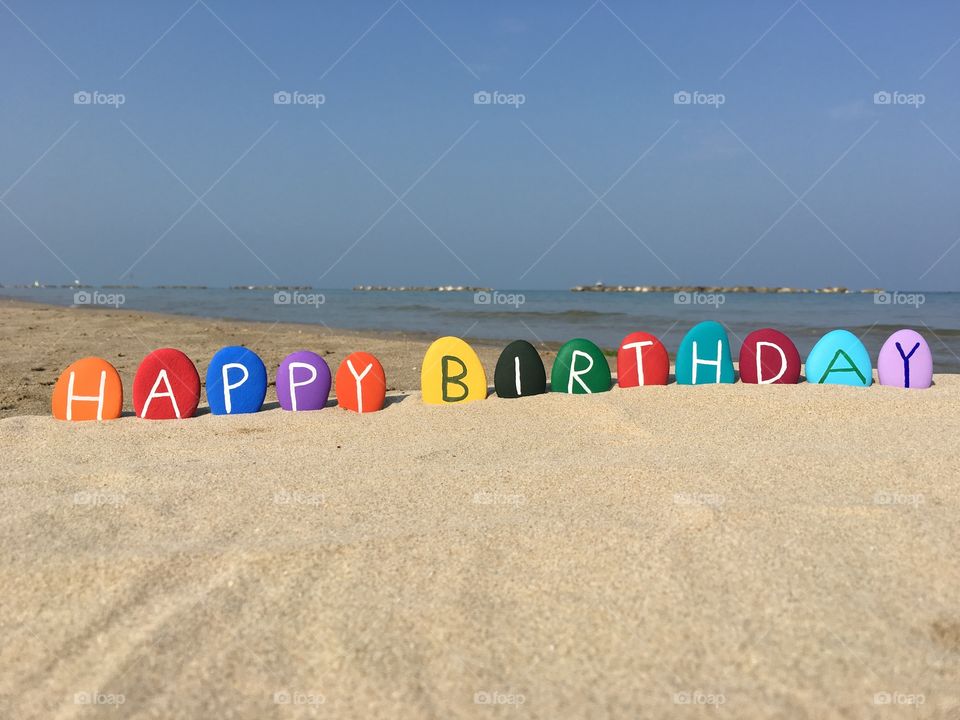 Happy Birthday on colored stones with beach background
