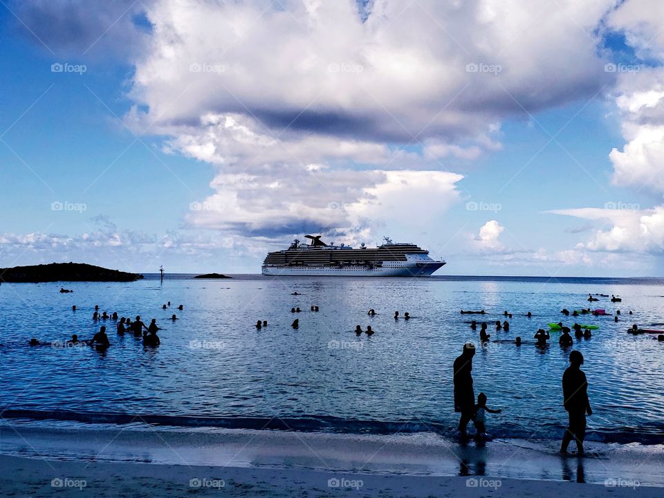 A cruise ship is seen in the Caribbean Ocean of Grand Turks, Caicos Island. People are silhouetted against the blue ocean and sky.