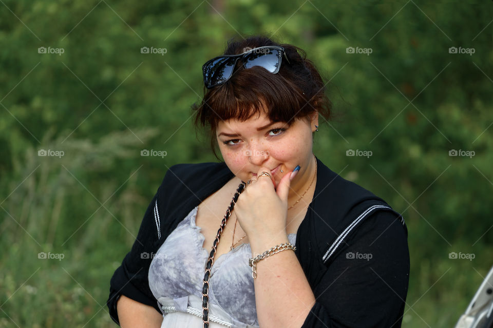 Portrait of a young girl with glasses and sly squint on the background of green forest on a sunny summer day