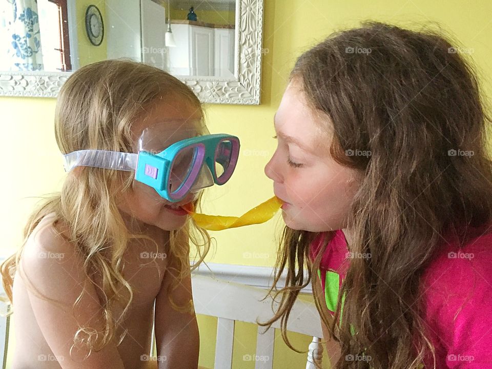 Two silly sisters sharing a fruit by the foot snack. 