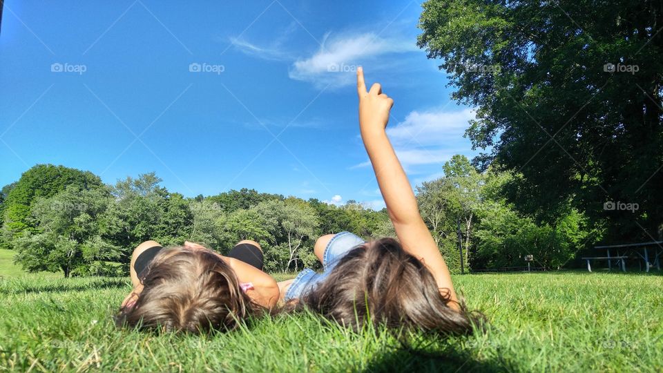 Two girls lying on grass pointing towards sky
