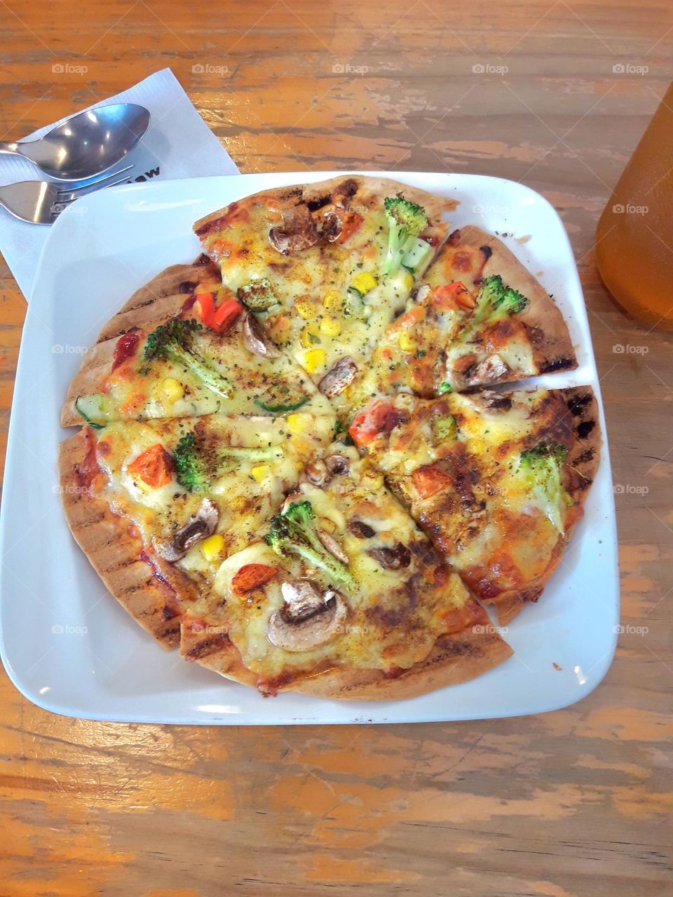 Thin crust pizza with mushrooms and broccoli and corn and tomatoes and cheese