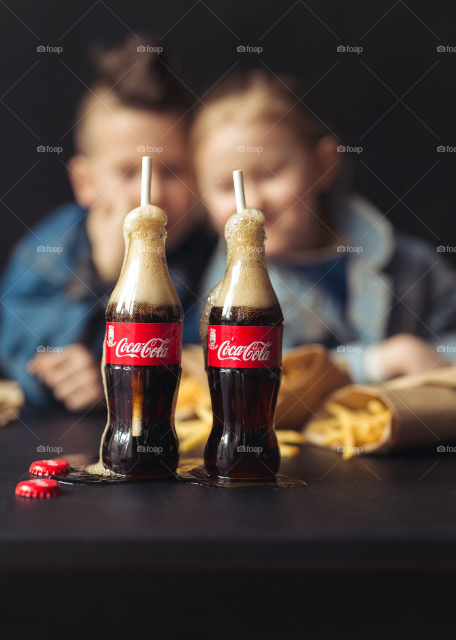 a boy and a girl of seven and five years old, friends, drinking Coca Cola, laughing, having fun, wearing denim clothes. Black background. Original photo. Nature product. Lifestyle photo