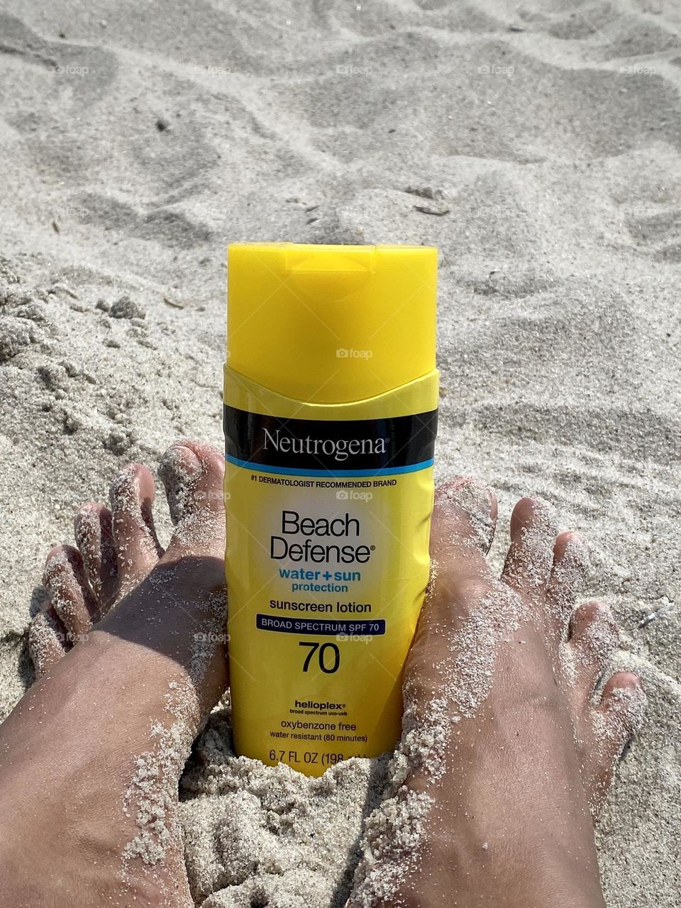 Person’s feet holding Neutrogena Beach defense water plus sun protection sunscreen lotion. 