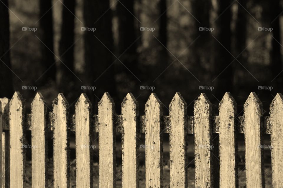 A sepia toned closeup of an old weather-worn wooden picket fence at a Japanese-Chinese cemetery. 