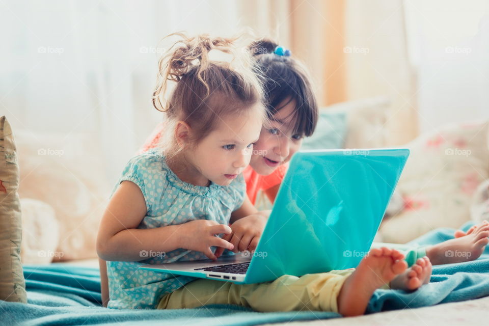 Little sisters with gadgets(laptop and tablet) in the bed.