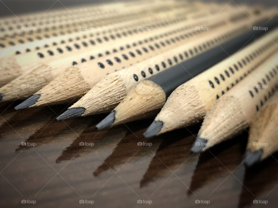 Pencils on the table. Same graphite color, but different wood-cases. A black pencil case among the brown ones...