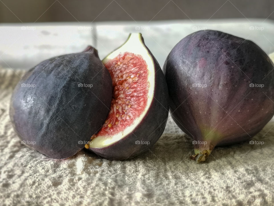 Two ripe fresh figs, one of which is cut in half, lie on a linen napkin on a table with a wooden surface.