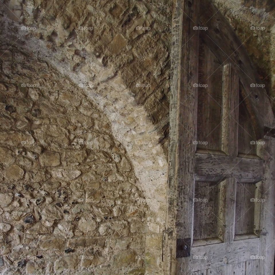 Unique texture of a very old brown stone wall with an equally textured wooden door built in in Europe. 