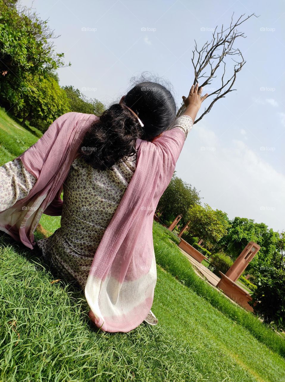 A woman trying to touch the dry tree in the park from the ground