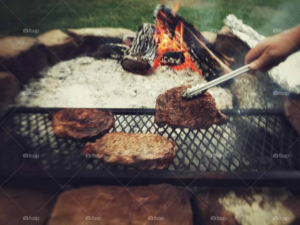 Steaks being cooked over an open fire pit American traditional favorite dish