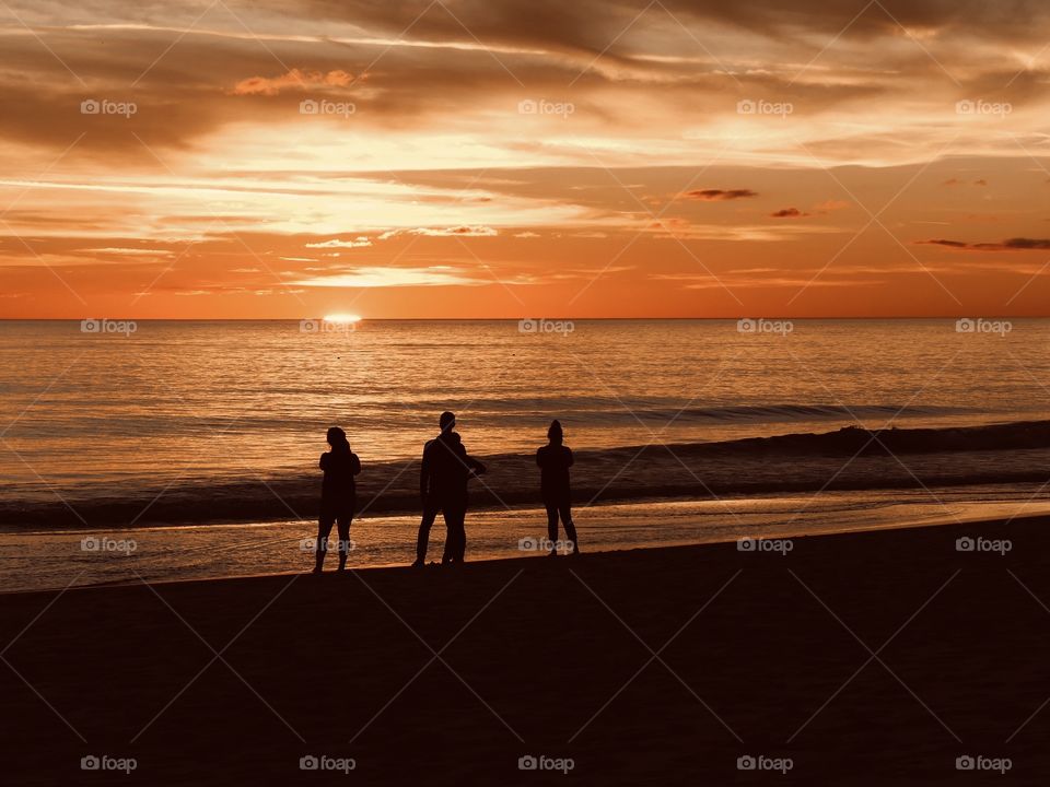 A family is walking along the beach in front of the Gulf of Mexico and enjoying the sunset