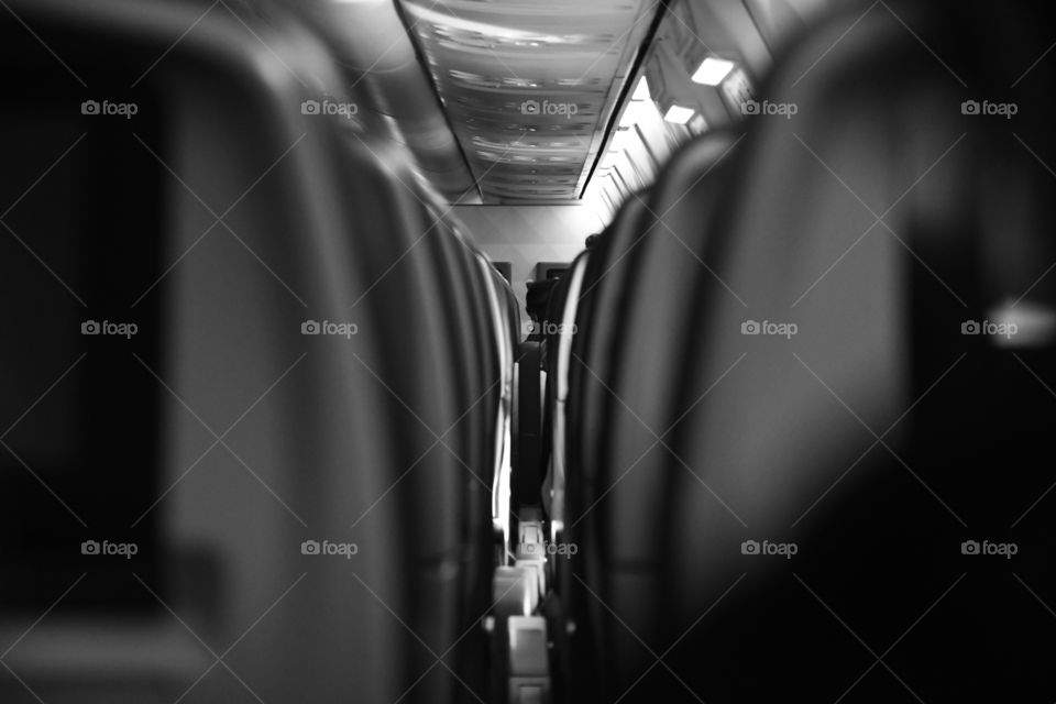 A black and white commercial airliner cabin point of the rows of seats in the aisle.