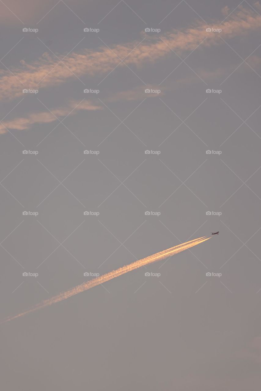 An airplane flying at dawn with a trail of engines