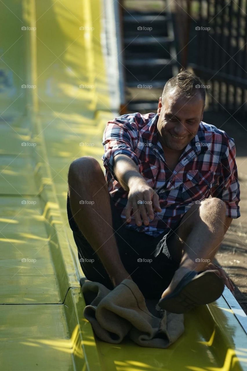 Happy man sitting on yellow slide in water park