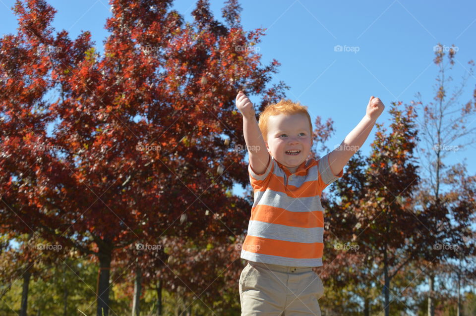Little boy with arm raised against autumn tree