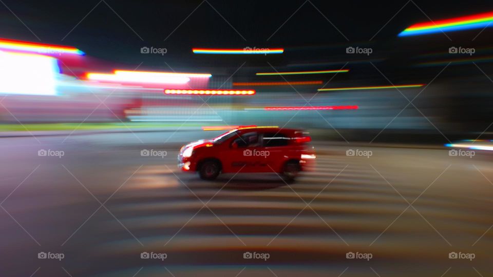 A dynamic red car in motion at night, with vibrant neon lights and motion blur creating a sense of speed and energy. The streaks of light and the car's vibrant color add a modern and urban vibe, perfect for themes of transportation.
