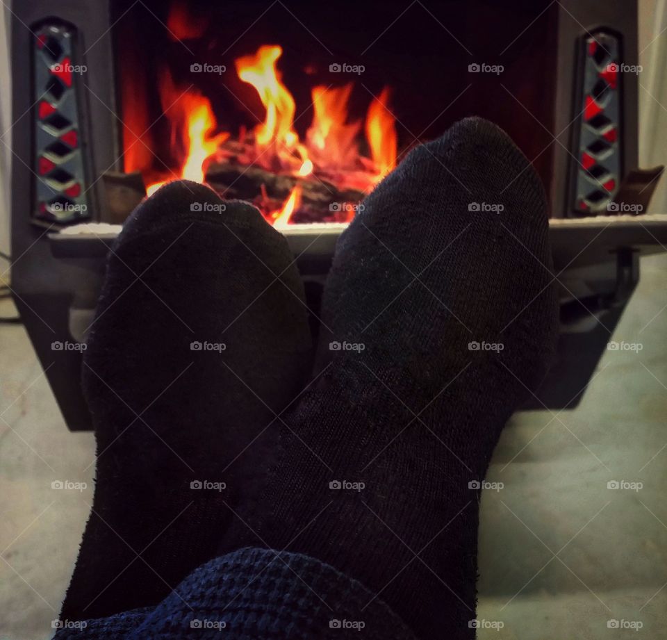 Sock feet in front of a wood burning stove with a cozy fire relaxing in winter