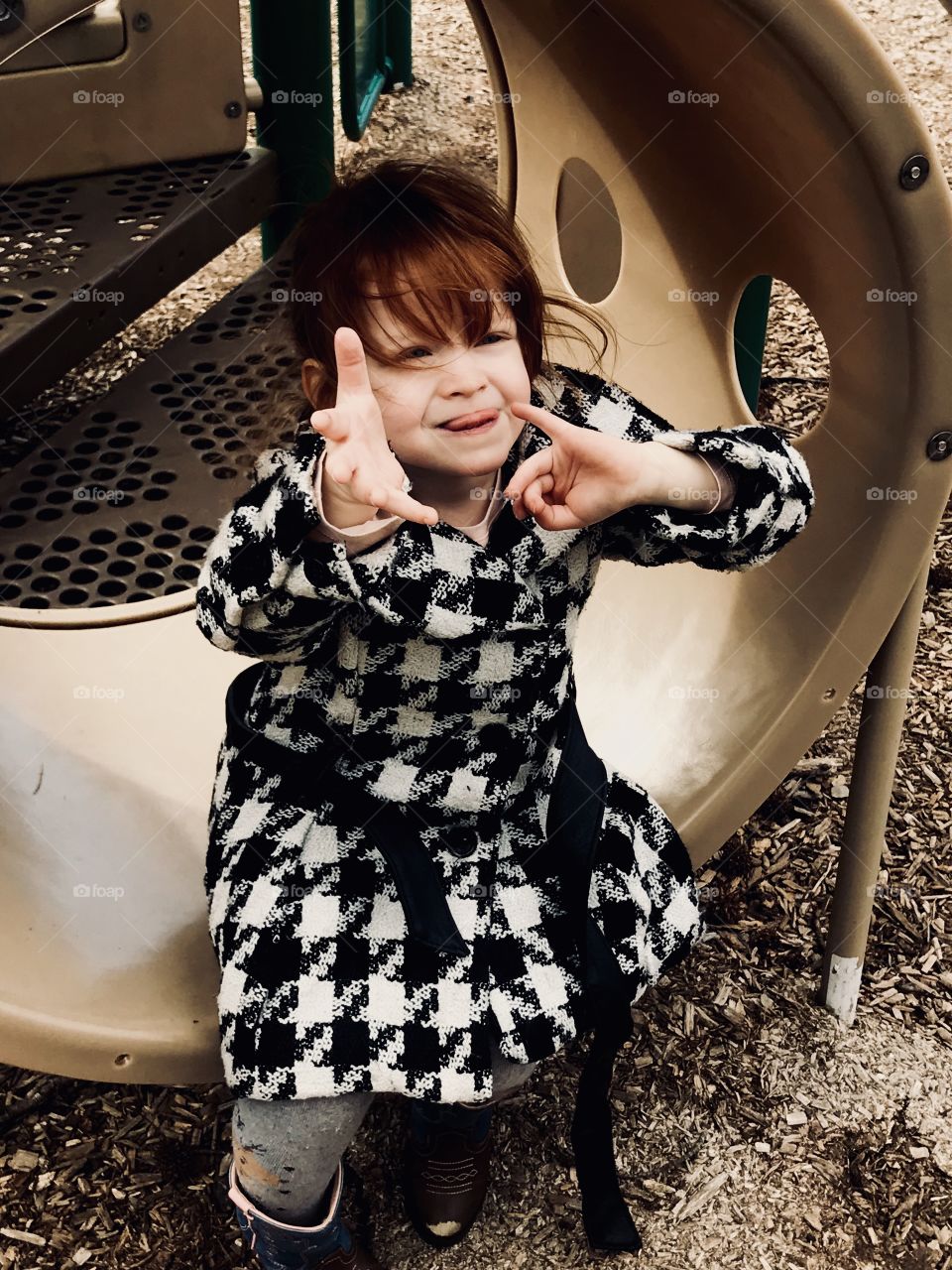 Beautiful red haired girl acting goofy and having fun at our local playground. Wearing a black and white coat and looking dashing. 