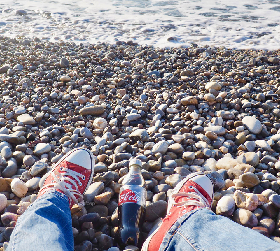 A bottle of Diet Coke on the beach in Nice with red sneakers.