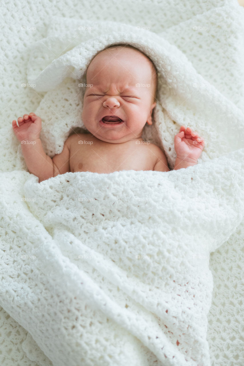 Newborn baby boy crying in blanket not happy