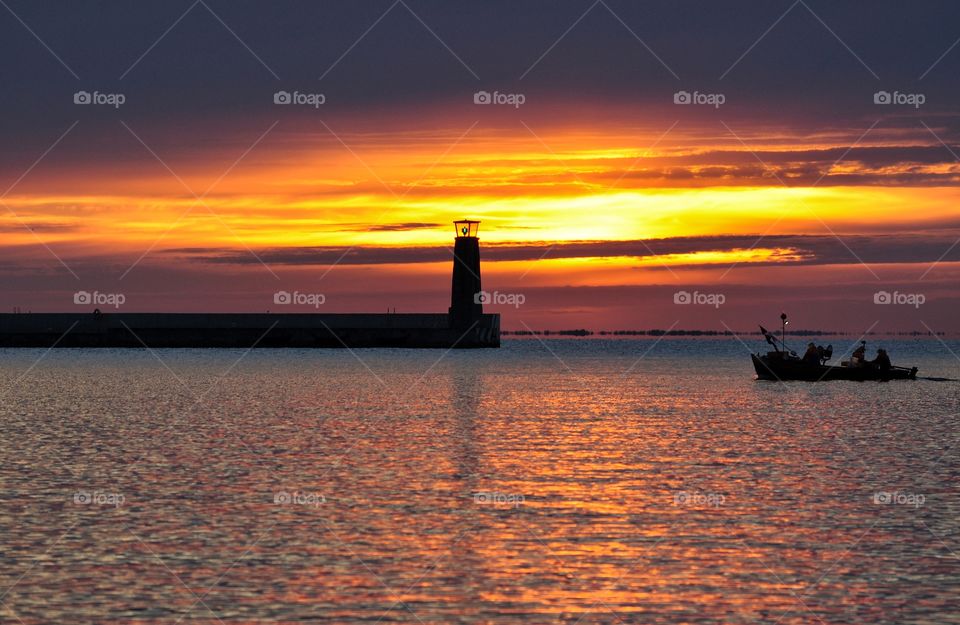 fishermen boat in the baltic sea near the lughthouse on horizon during sunrise in gdynia, poland