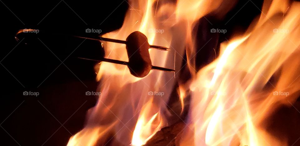 A plump hot dog over the fire.