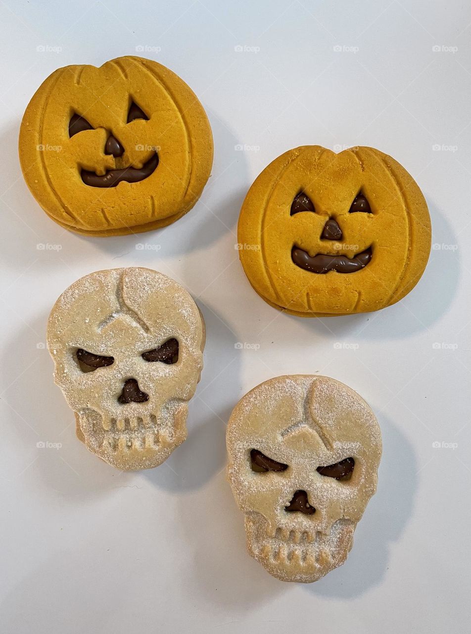 Pumpkins and skulls shaped Halloween freshly baked cookies against white background 