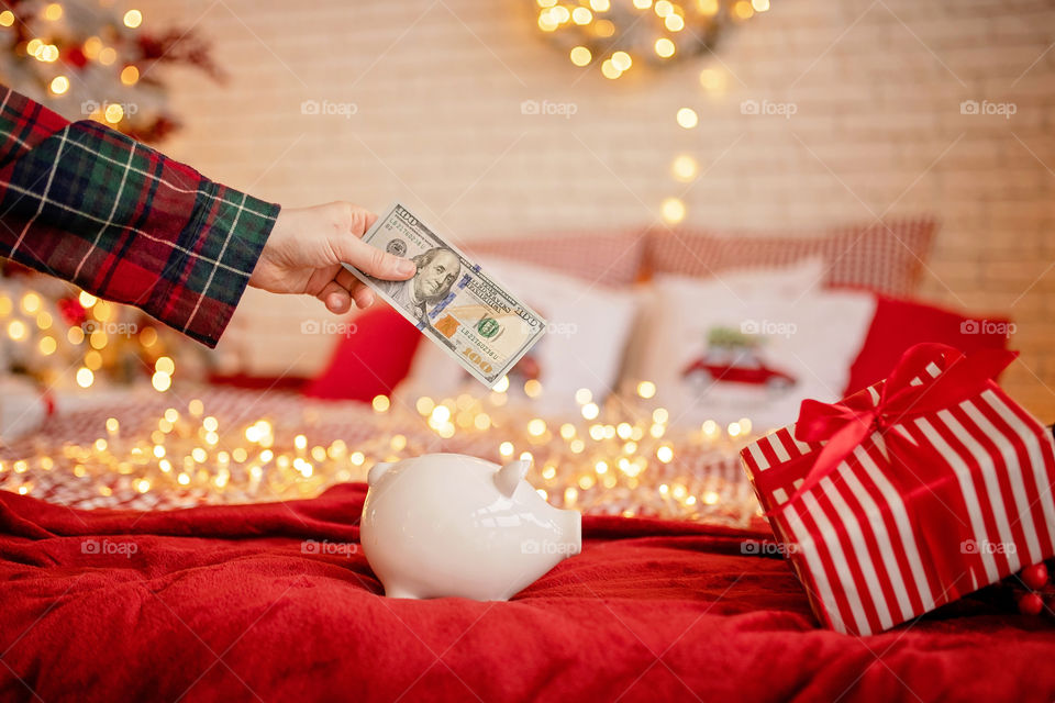 piggy bank with 100 dollars banknote in festive New Year atmosphere of scenery.  Magical bokeh with Christmas tree and bright lights.