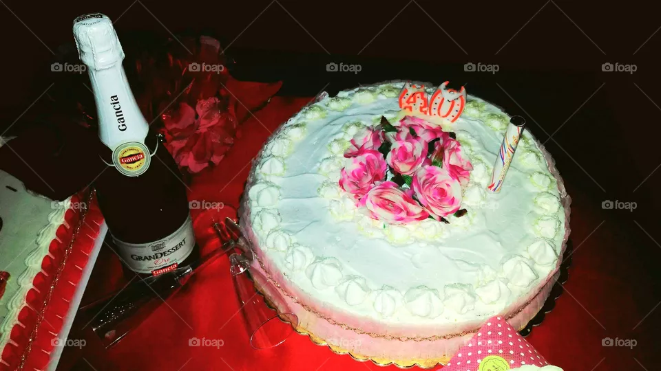 A 40th birthday rose cake with a bottle of Italian bubbly wine on a red tablecloth and red flowers