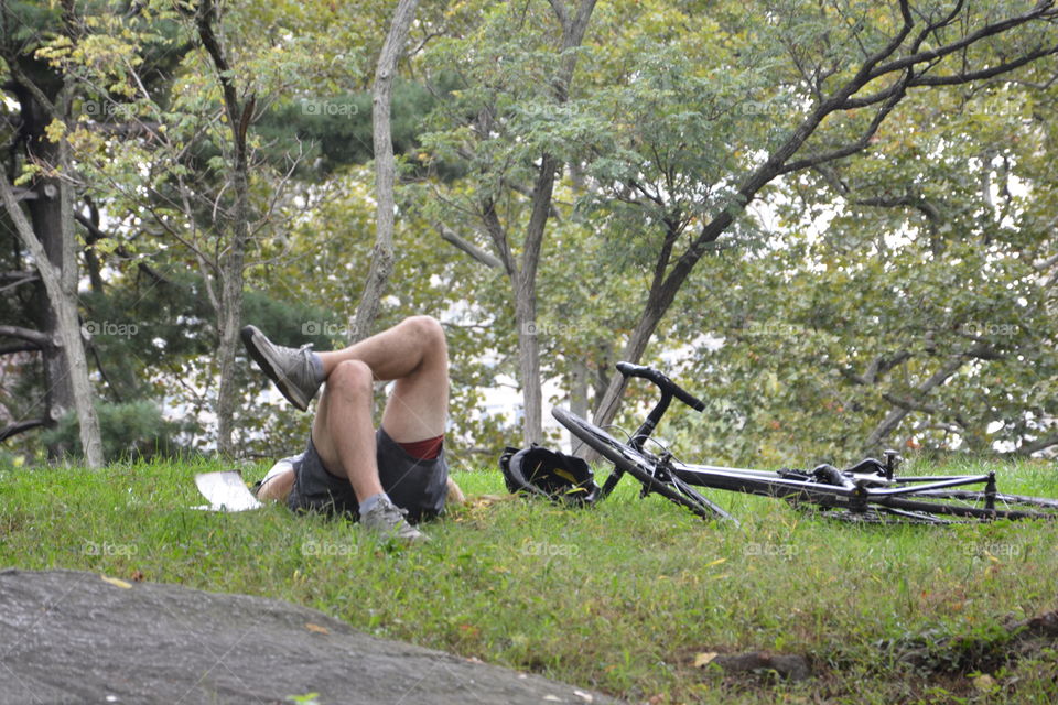 Add adult unrecognizable male lays on the grass with his bike beside him in a park