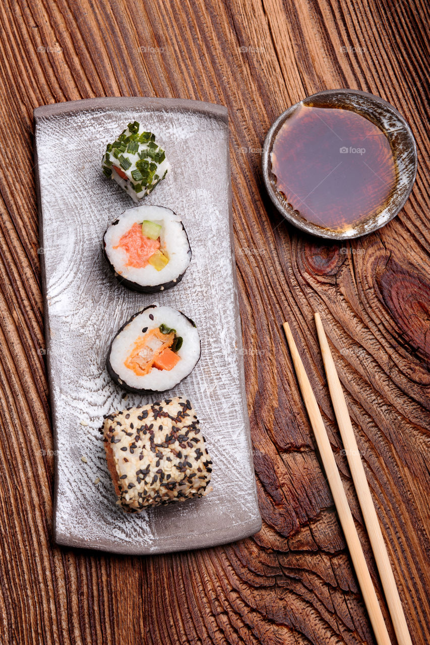 Sushi set on pottery plate with chopsticks and soy sauce in bowl on old wooden table from above