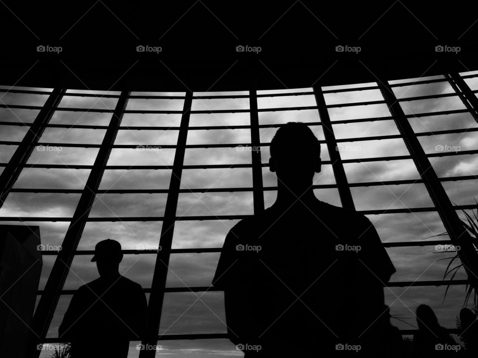 Silhouettes against a large window with sky. Ominous silhouette of two people standing against an airport window