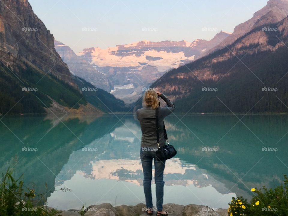 Female photographer at lake Louise in Banff National Park, Alberta Canada, photographing snow capped mountains and reflections on lake