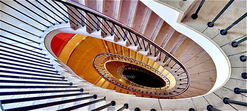 The elliptical spiral staircase in “Munich”, Germany in its actual orientation which is sideways looking down from the higher floors at the metal railing twisting and bending its way downward. 2022. Hypnotic Productions