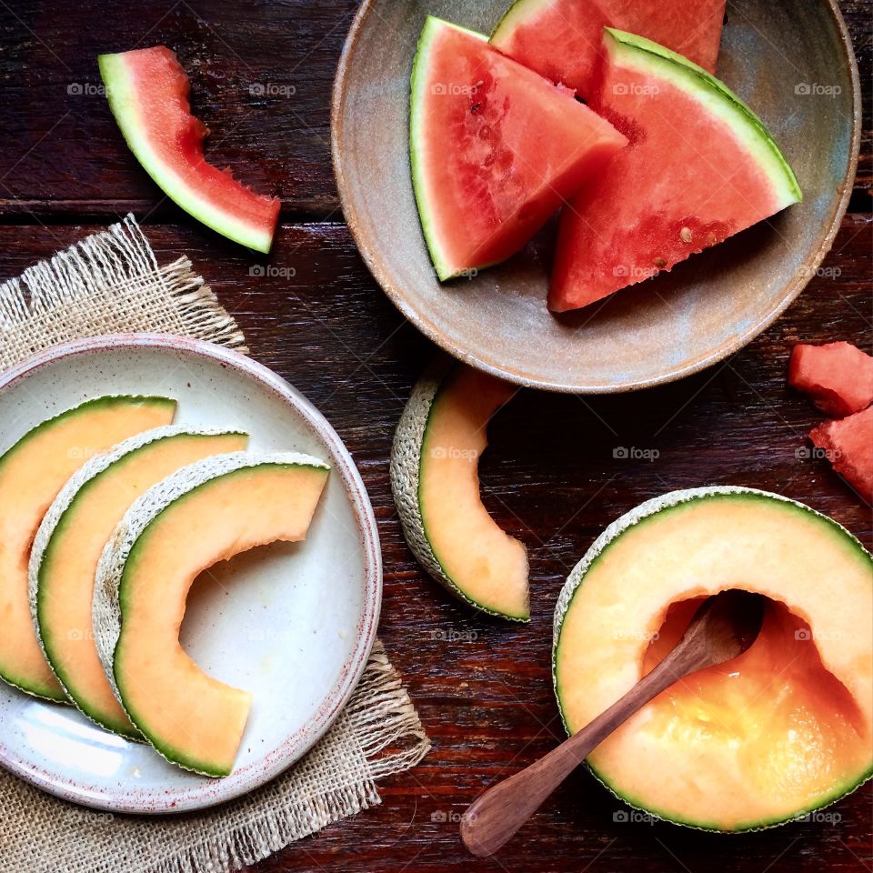 Sliced watermelon and cantaloupe on ceramic plates  sitting on rustic wood table.
