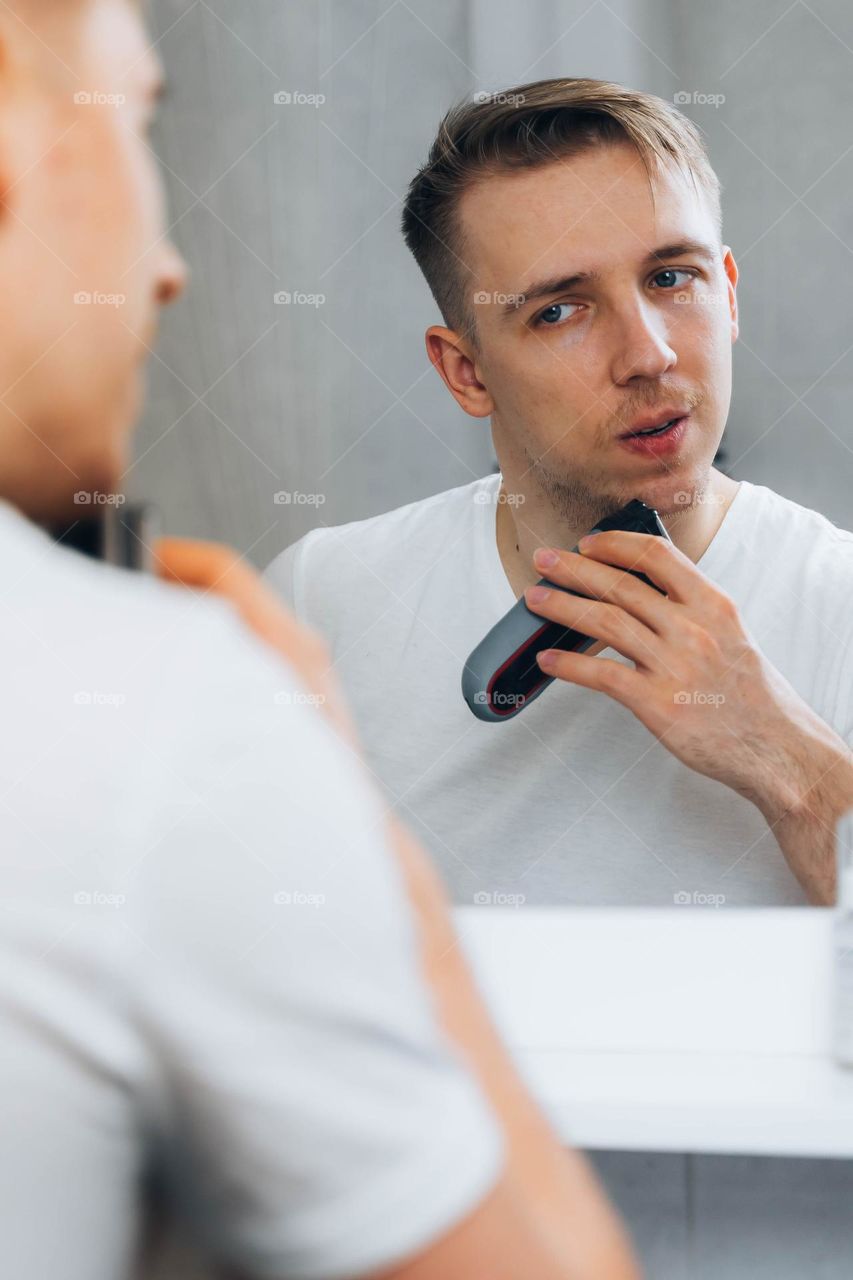 Man shaving his beard in bathroom using electric shaver 