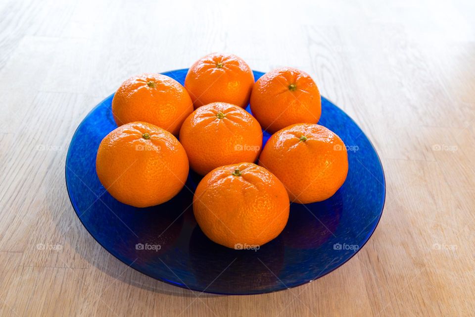 Blue glass plate with bright orange colored clementines fruits on a kitchen table 