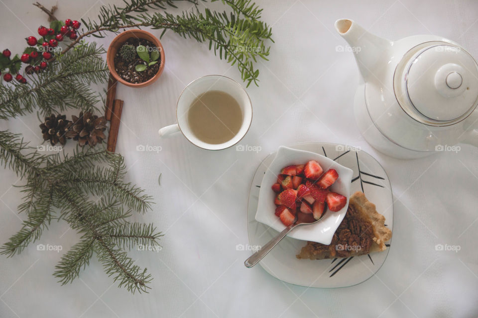 Tea, strawberries and pecan pie beside a teapot in a festive flat lay.