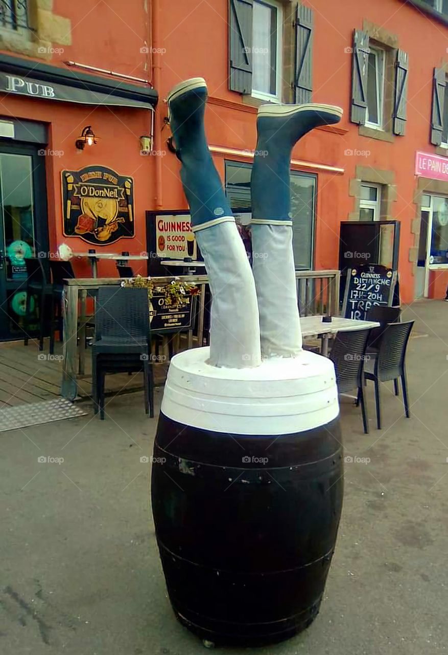 A pair of booted legs sticking out of a pint of guinness outside a pub