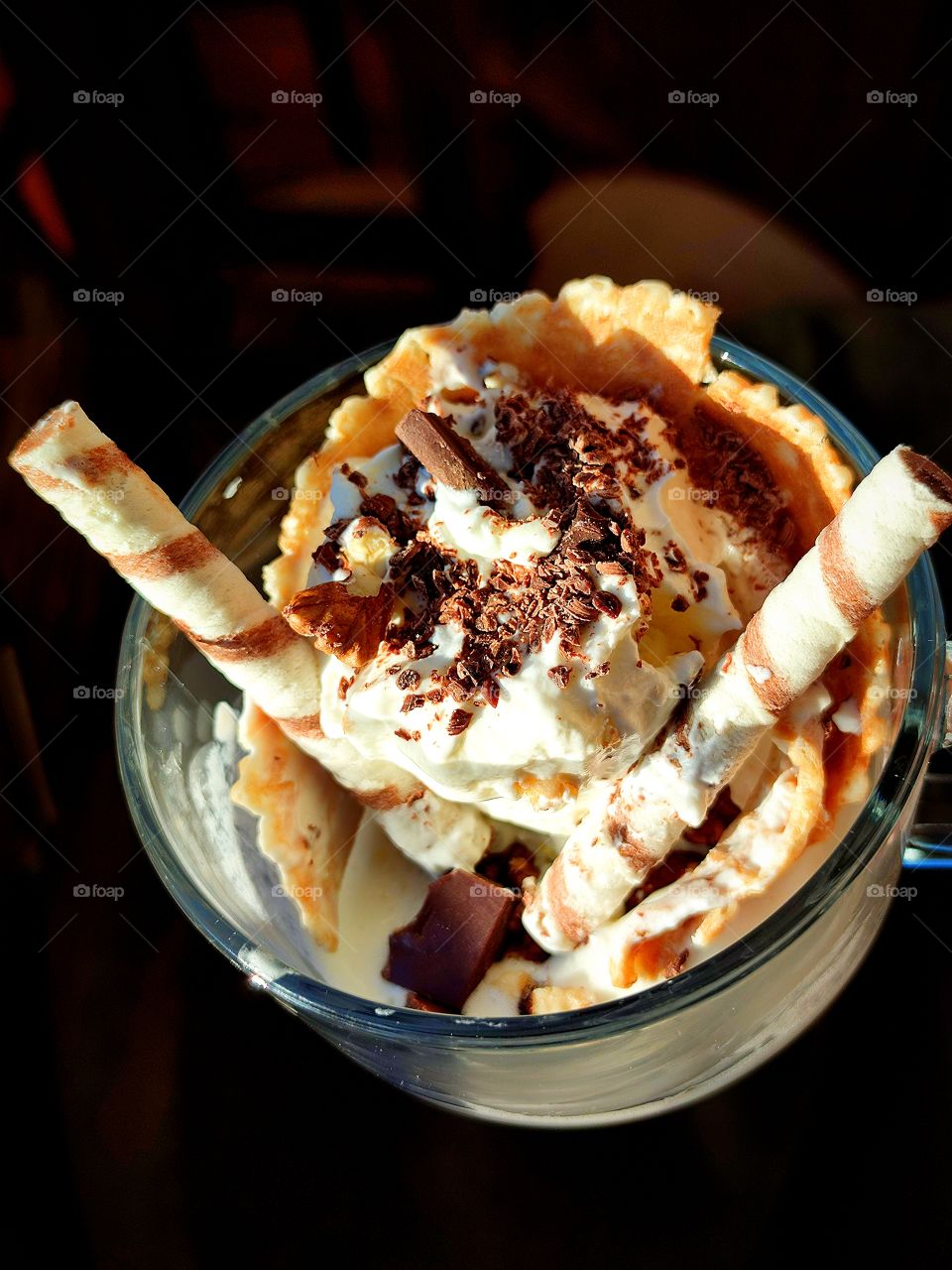 The cup contains ice cream sprinkled with chocolate chips and nuts.  Wafer rolls are inserted into the ice cream