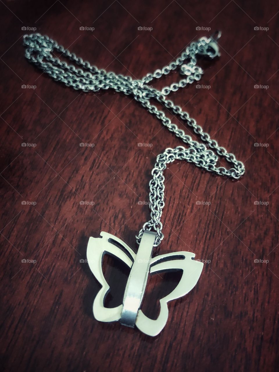 A silver necklace with a butterfly as a pendant. Taken off for the night, resting on a wooden table.