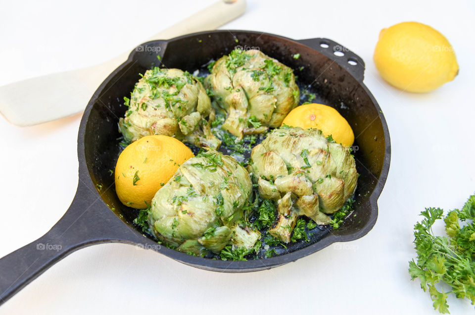 Close-up of roasted artichoke hearts and lemons in a cast iron skillet