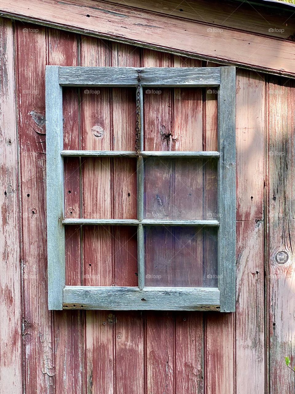 A window frame missing several panes of glass on the side of a wooden structure 