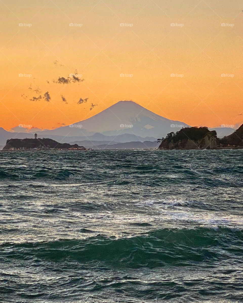 Mt Fuji encased by orange sky and ocean, with Enoshima island to the left. Blustery windy winter afternoon, looking relatively calm in this shot. Kamakura, Japan