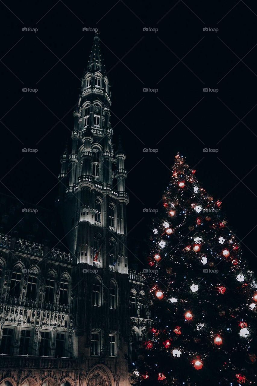 Beautiful night view of the glowing spire of an ancient castle with a Christmas tree in the city of Brussels on the grand place in Belgium. Concept of christmas, new year.