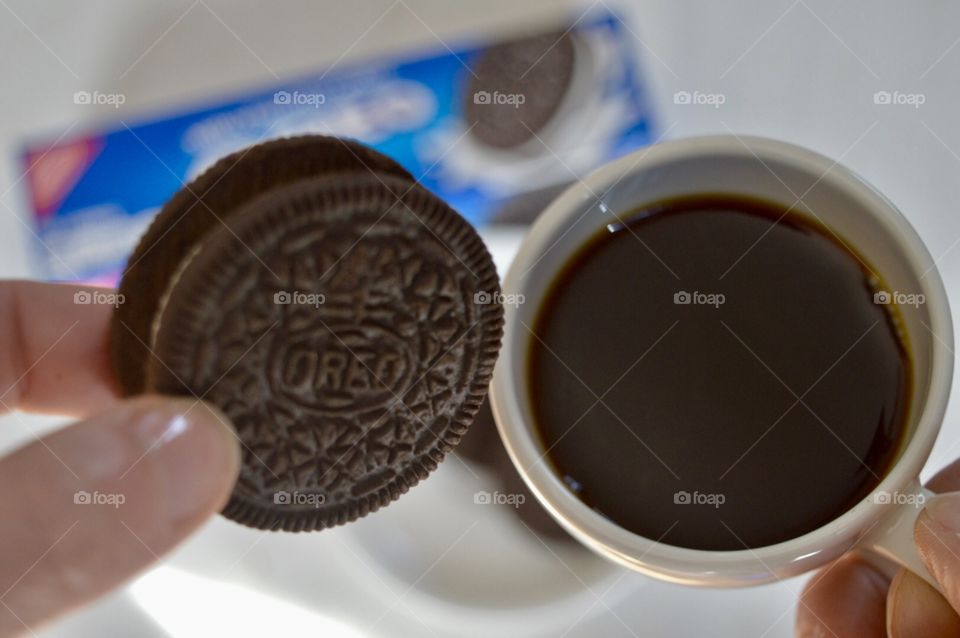 A person’s hand holding an Oreo cookie and a cup of coffee